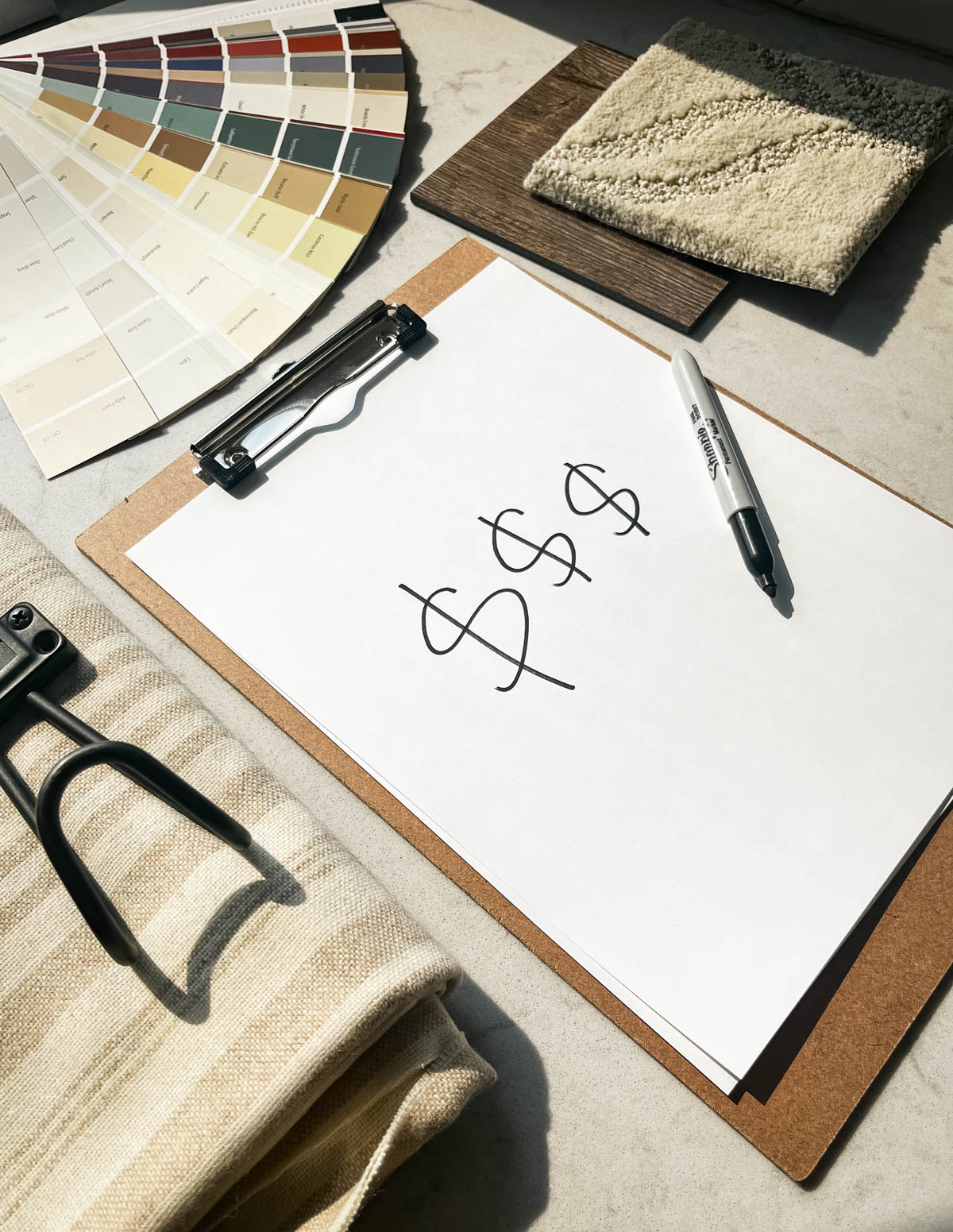 clipboard with dollar signs in sharpie, surrounded by room makeover supplies and samples