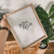 shake your shamrocks hand lettered art in a frame, held in front of plants