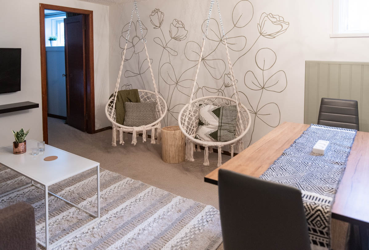 hanging chairs in front of a green floral line art mural