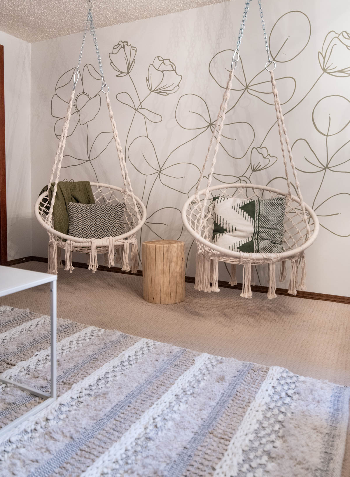 hanging chairs in front of a green floral line art mural